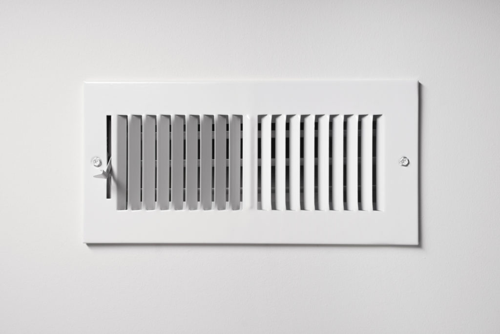 A HVAC vent register on the wall of a home, with a lever that can open and close. 