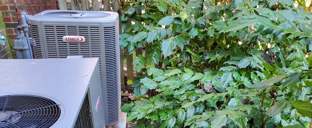 Picture of the outside unit of the HVAC system next to some shrubs for our Fall Checklist blog.