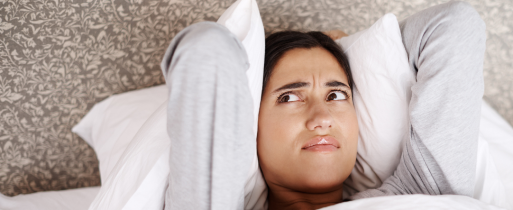 Stock photo of a woman covering her ears with her pillow from Canva for our Why Does My Furnace Smell And Other Questions blog.