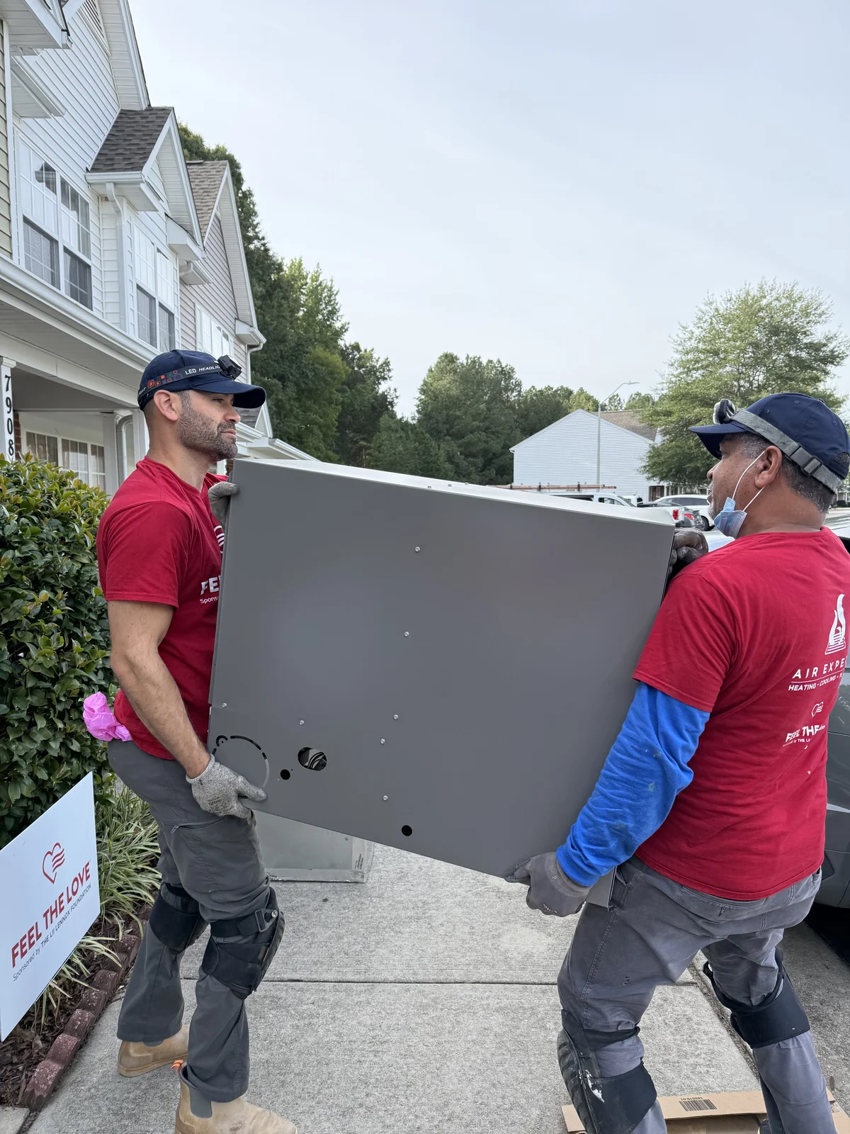 Two Air Experts technicians carrying the old, failing HVAC system out of the home