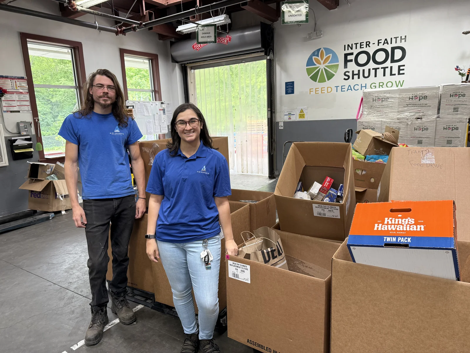 Two Air Experts employees inside the Inter-Faith Food Shuttle warehouse with donated boxes