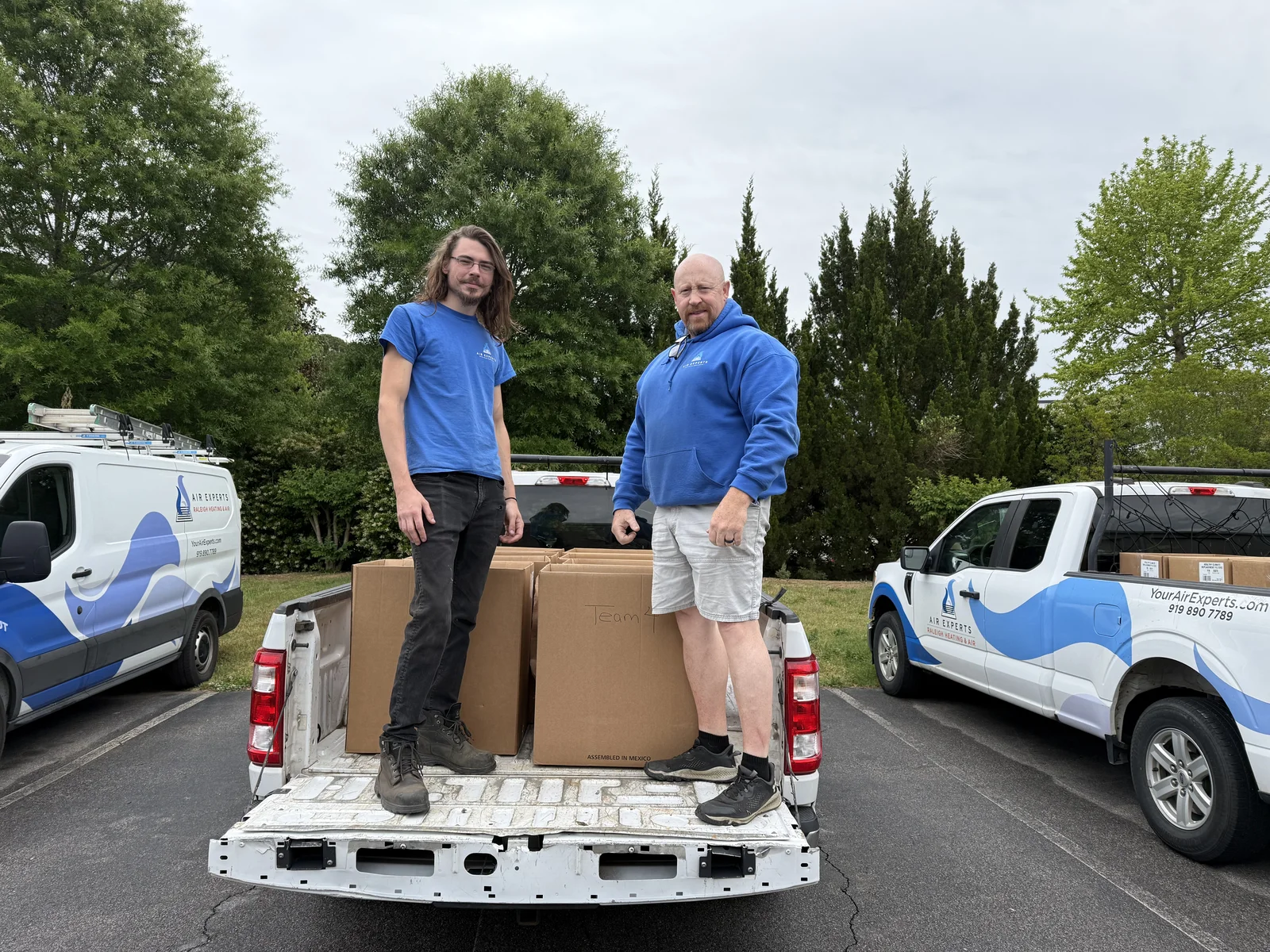 Two Air Experts employees standing in a truck bed loaded with donated food boxes