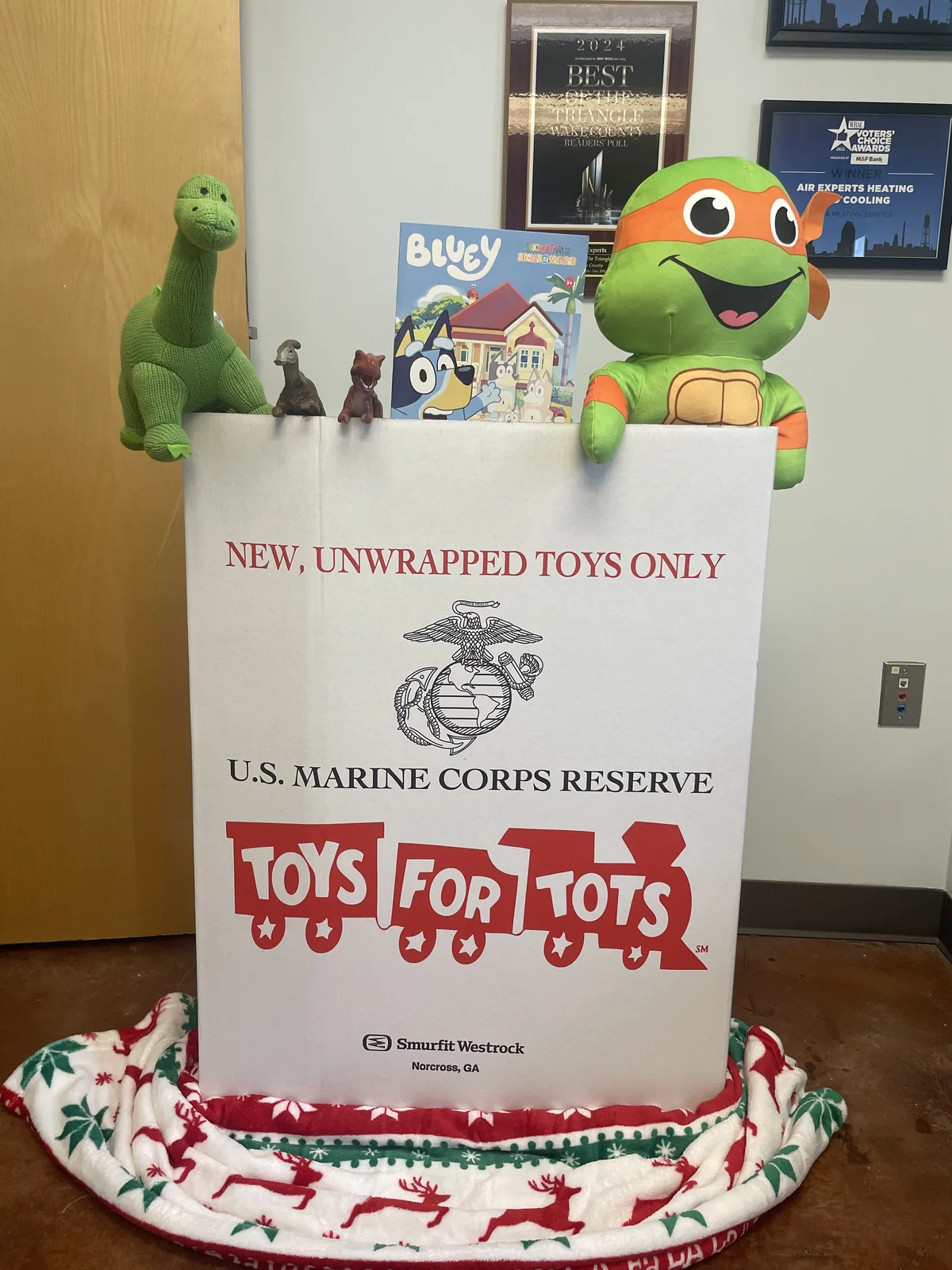 Official Toys for Tots collection box decorated with toys at the Air Experts office