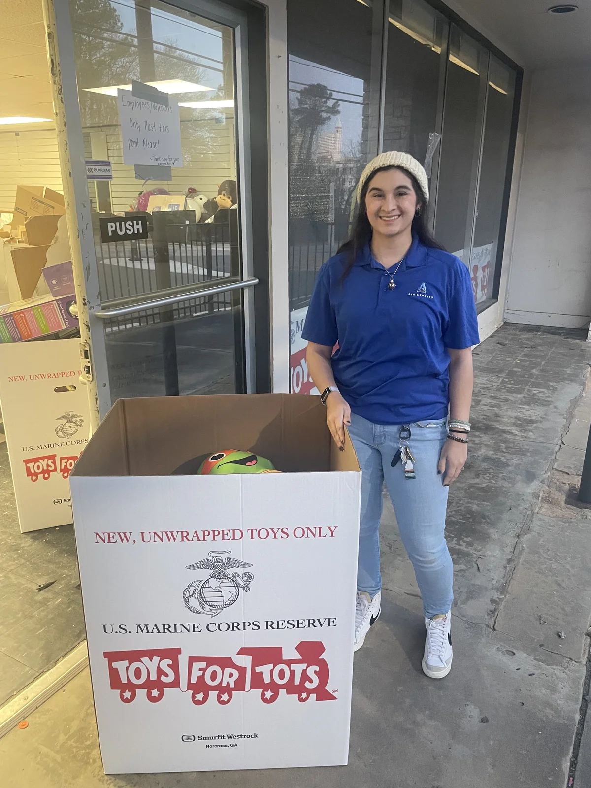 Air Experts employee standing next to the Toys for Tots collection box at the office entrance