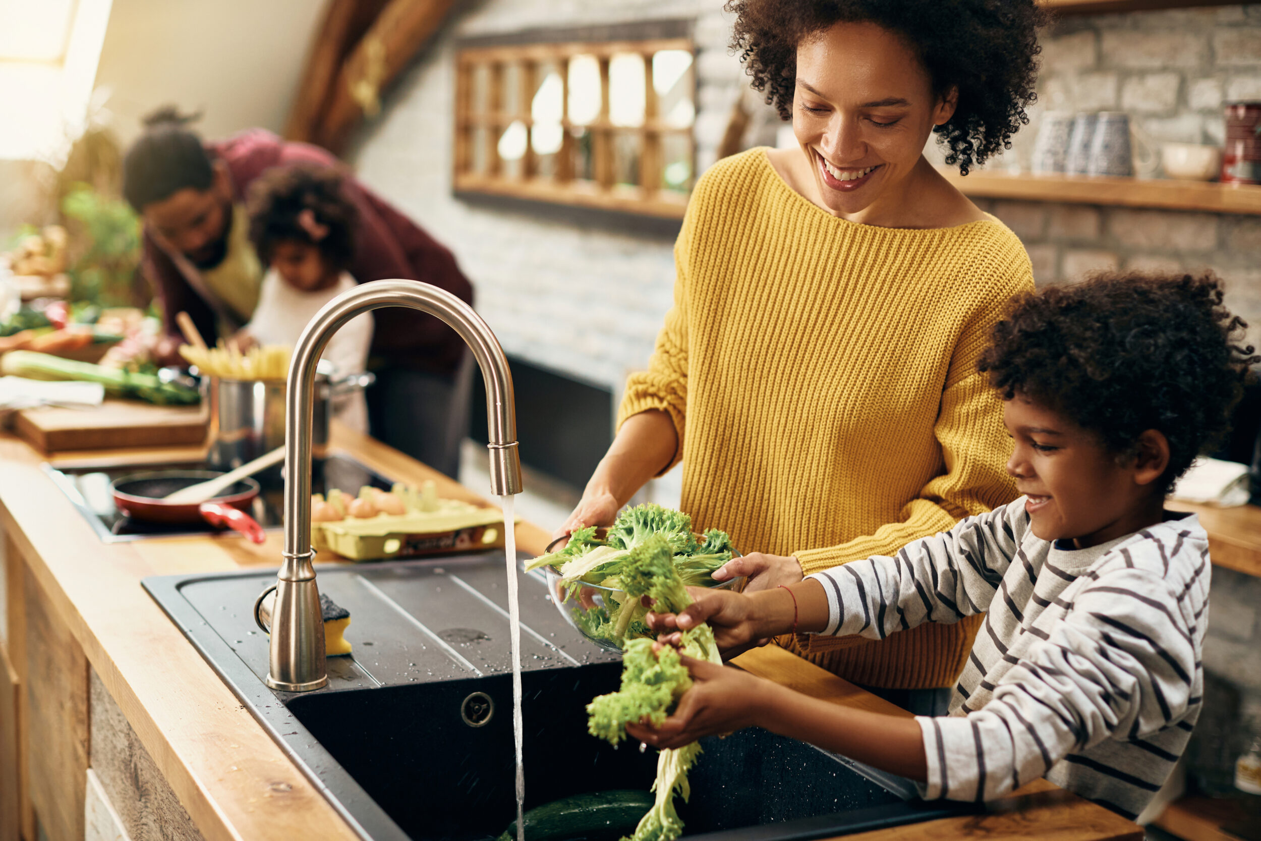 Mother and son standing at the kitchen sink with father and daughter in the background.